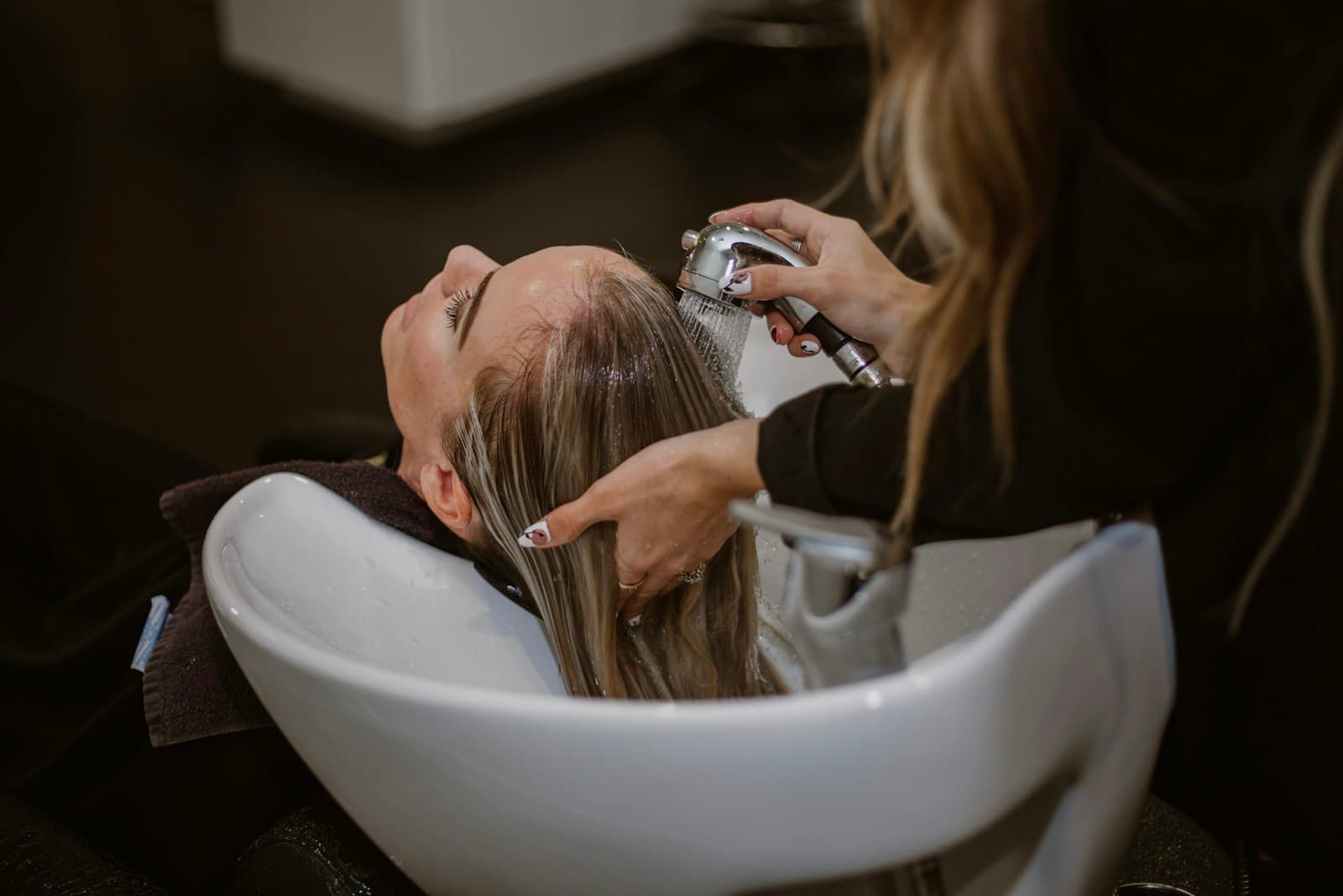 A stylist rinsing a client’s hair at the basin